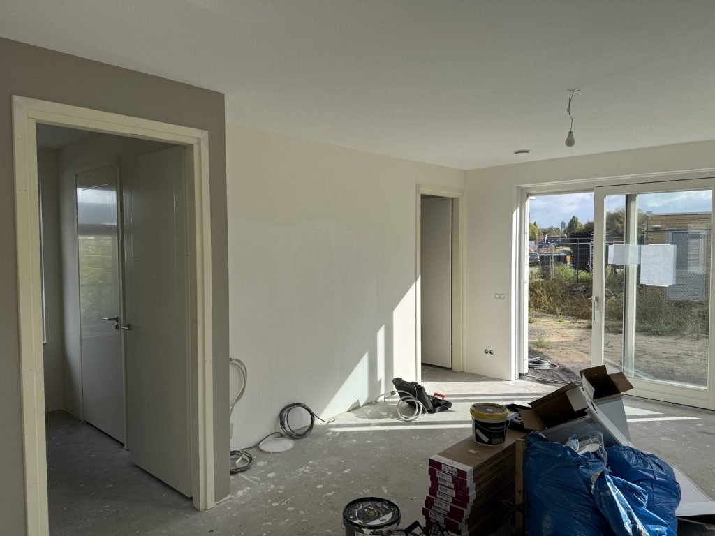Net opgeleverde nieuwbouwwoning met kale wanden, verfemmers en dozen op de betonvloer