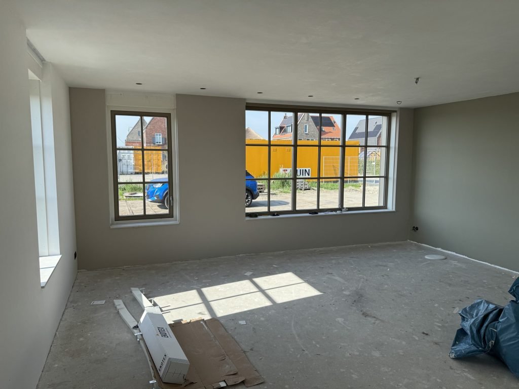 Lege kamer in een nieuwbouwwoning met kale grijze wanden en een groot raam met roeden