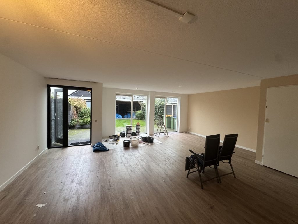 Woonkamer van een rijtjeshuis met lichte wanden, een houten vloer en tuindeuren