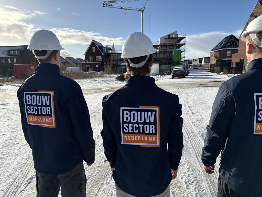 Drie vakmensen van Bouwsector Nederland met witte helm in een straat met nieuwe woningen in de sneeuw